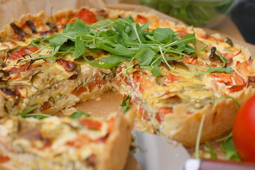 Arugula, goat cheese, sun dried tomato and prosciutto tart with a slice being removed