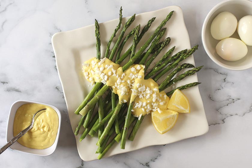 Asparagi di Bassano Con Salsa di Uova Sode (Asparagus with Egg Sauce) on a white plate with whole eggs and sauce in bowls beside it