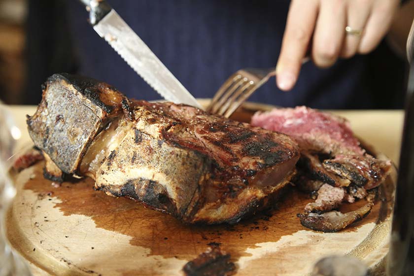 Bistecca alla Fiorentina (Florentine Steak) being sliced by a person holding a steak knife and fork