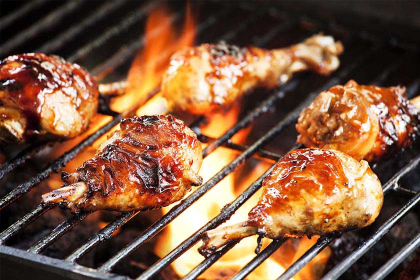 Braai style barbecue chicken roasting on a grill over open flames