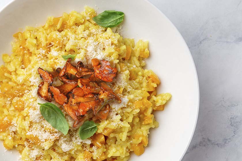 Bowl of butternut squash risotto topped with pancetta, chanterelle mushrooms, and Parmigiano-Reggiano