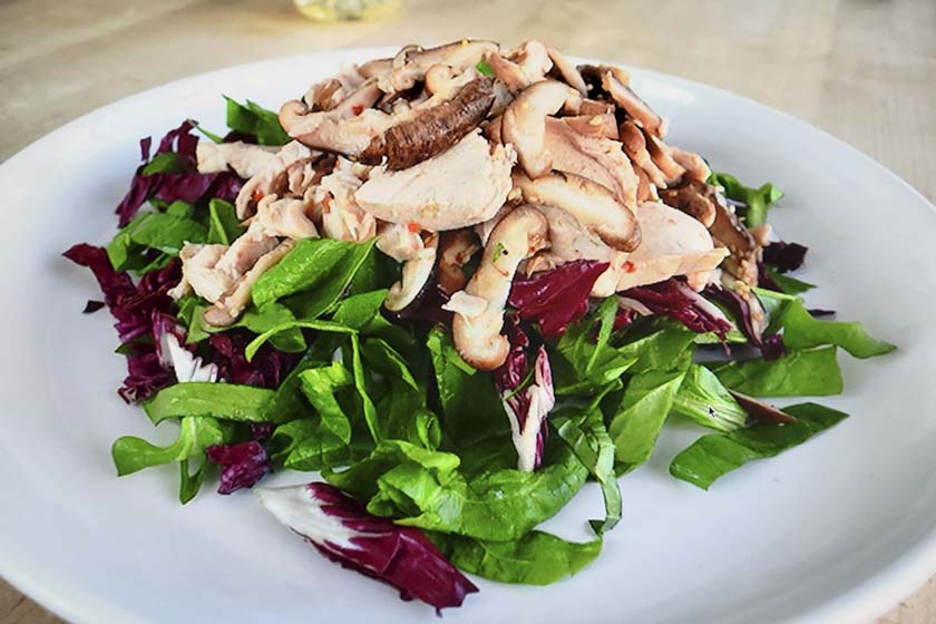 Roast chicken salad with spinach, scallion, and mushrooms on a white plate