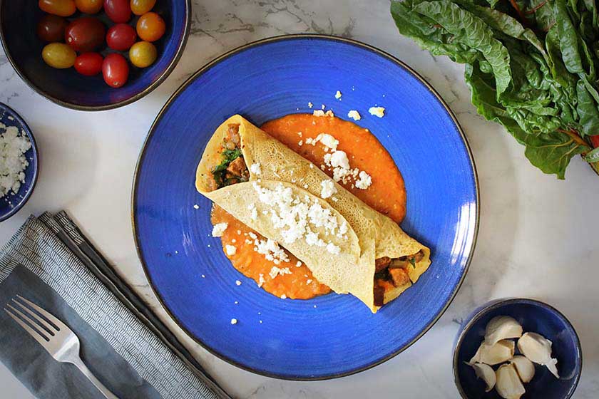 Chickpea crepes stuffed with swiss chard laying on cherry tomato sauce and topped with feta cheese