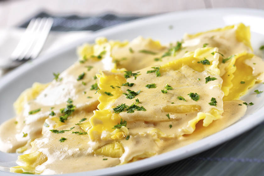 Crab ravioli with lemon butter sauce topped with chopped parsley on a white plate