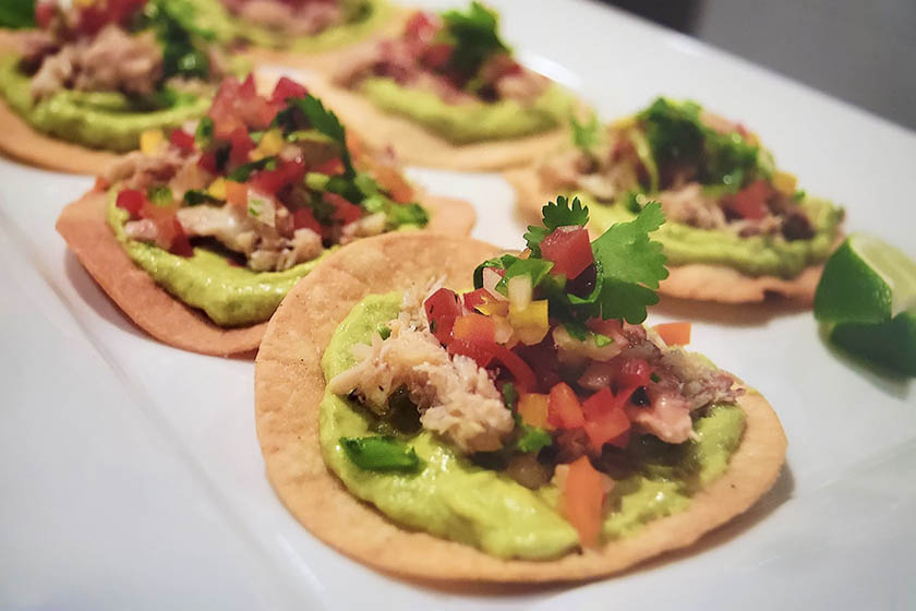 Close up of mini crab tostadas lined up on a white appetizer plate