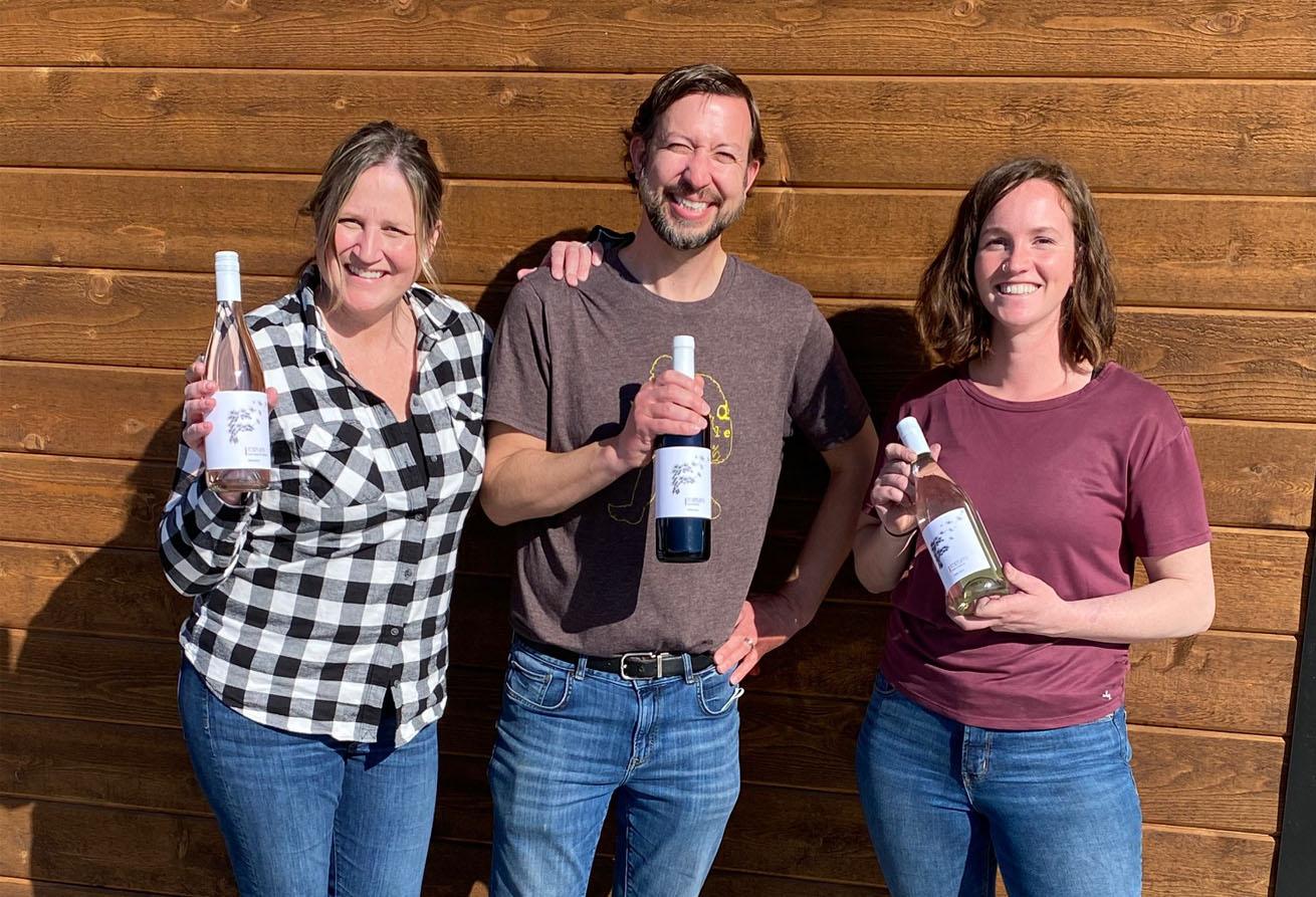 Fortuity Cellars owners Lee and Emily Fergestrom and winemaker, Alexis Sells smile and hold their wine bottles