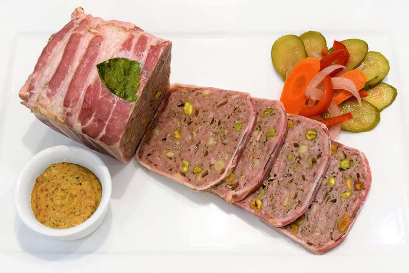 Pâté Campagne is wrapped in bacon with sides of pickled vegetables and whole grain mustard