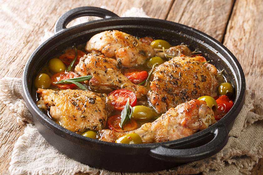 Roast chicken in a iron pot with tomatoes, olives, and broth