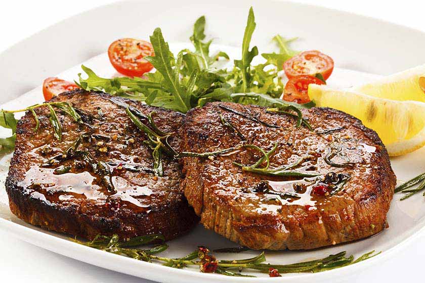 Two slices of balsamic glazed steak a la tagliatelle with arugula salad on a white plate