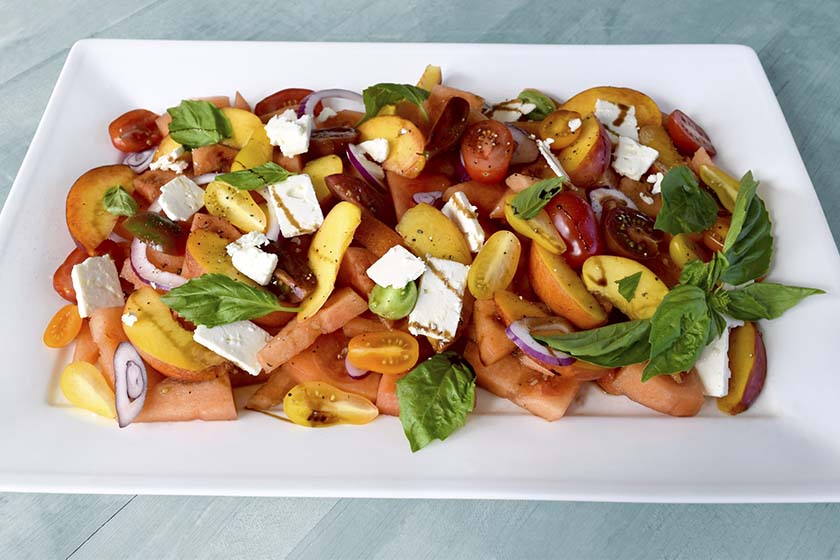 Watermelon feta salad with peaches, basil, and tomato on a white plate