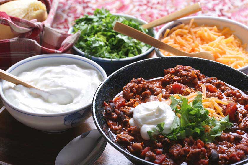 Bowl of game day chili surrounded by bowls of sour cream and shredded cheese