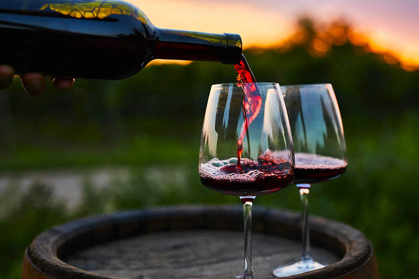 Cabernet Sauvignon being poured into two wine glasses in a sunset vineyard
